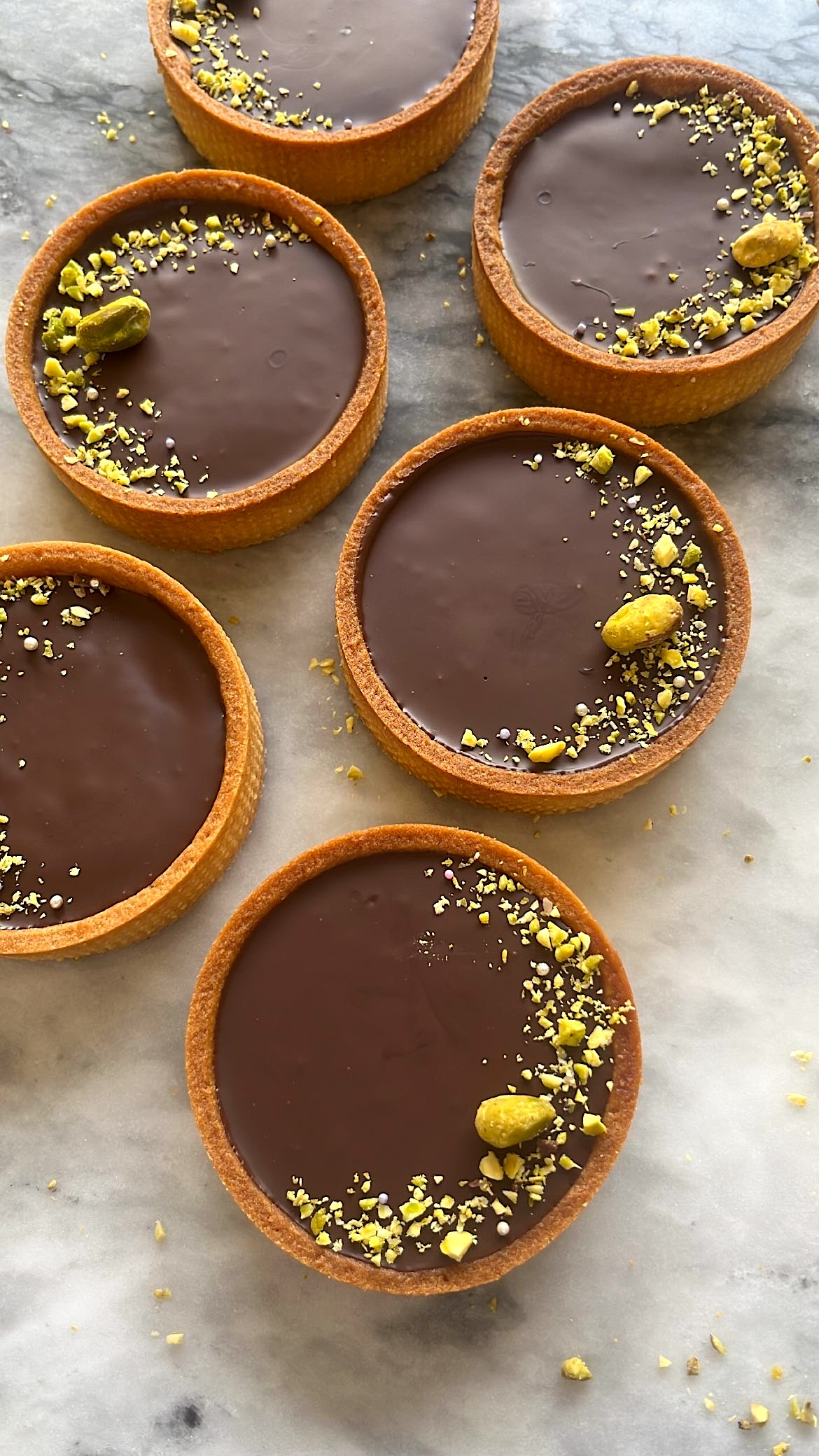 Chocolate tarts topped with sliced pistachios arranged decoratively