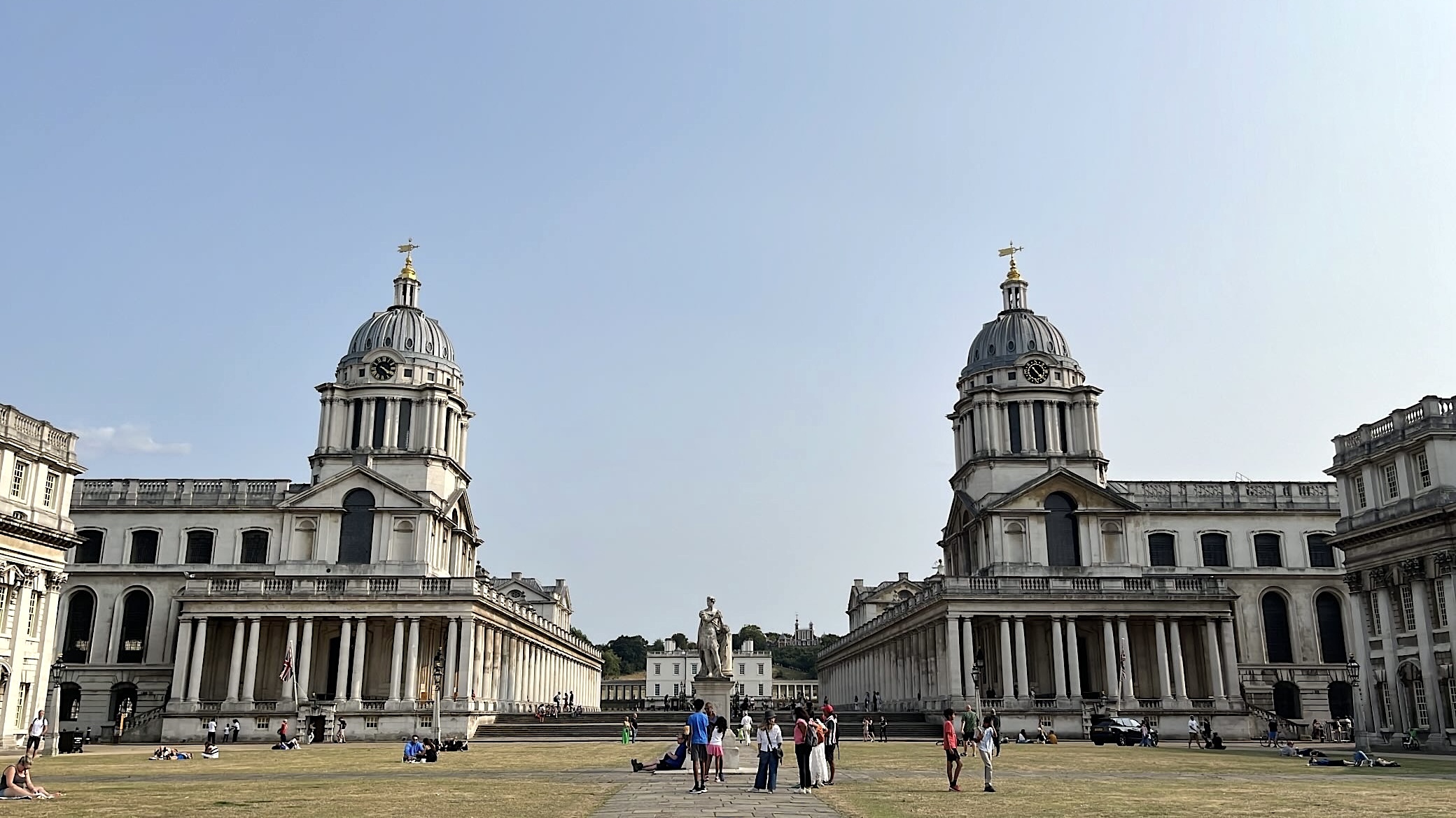 The two iconic domes of the Old Royal Naval College in Greenwich, with their symmetrical design standing against a bright sky.