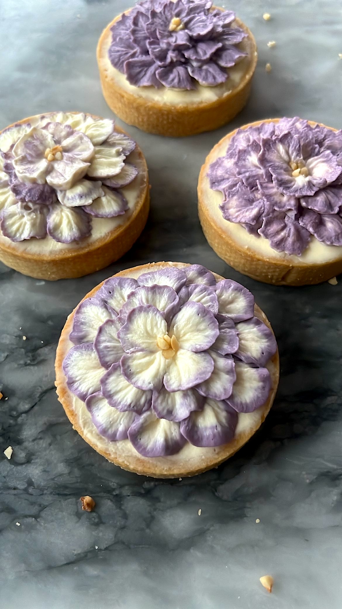 Three tarts decorated with purple and white flower-shaped cream piping on top